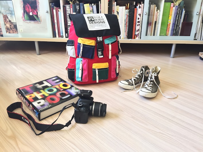 A vibrant backpack with multiple compartments resting on a school desk filled with books and supplies.