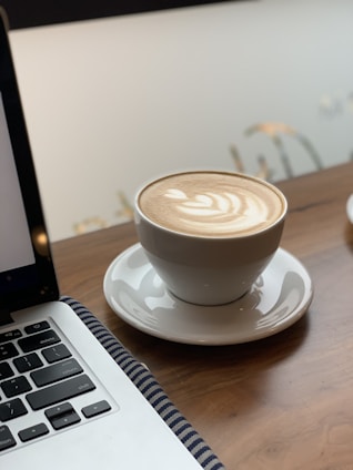 Warm coffee cup with latte art on a wooden desk beside a laptop in a bright coworking space