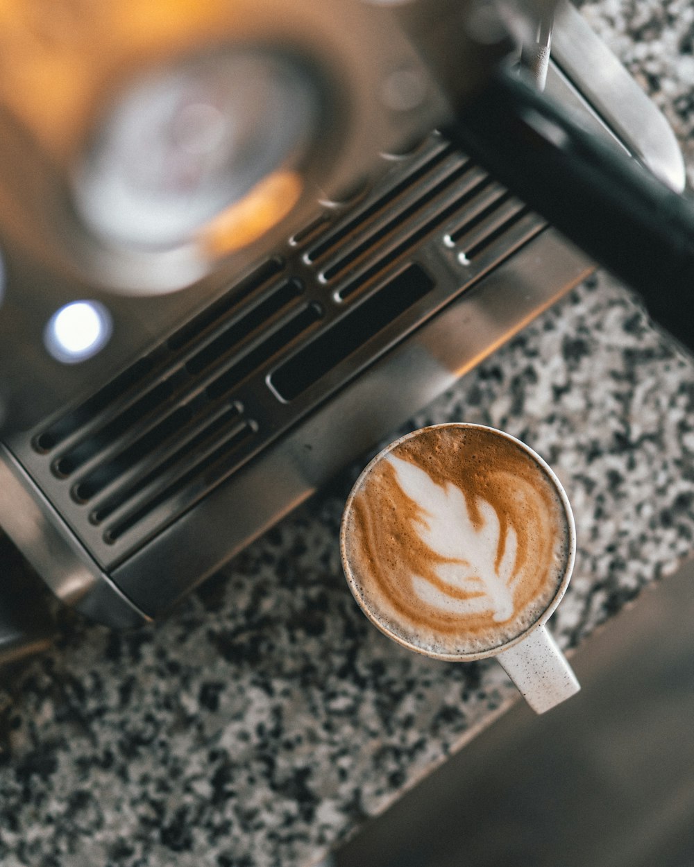 cappuccino in white mug near gray coffee maker