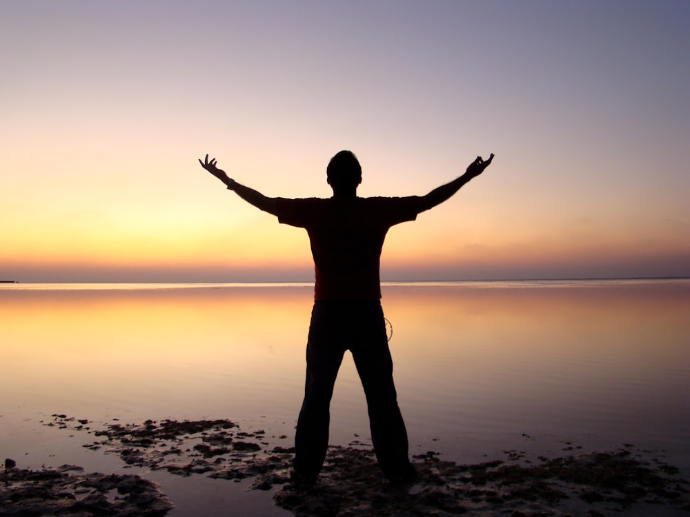 silhouette of person standing beside body of water