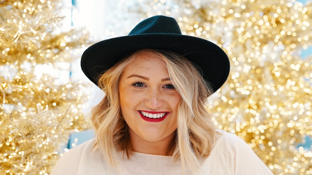 smiling woman wearing black fedora hat and white top