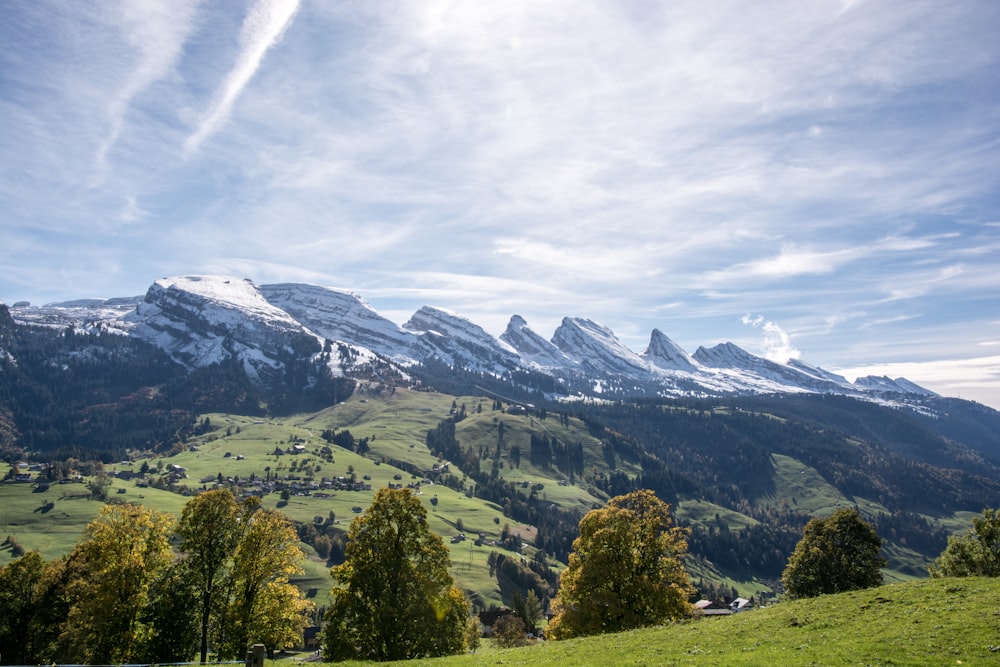 mountain and green field under white and blue skies