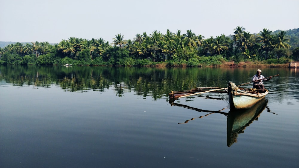 man sitting on boat on body of water near green trees during daytime