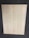 A large, rectangular piece of light wood with prominent grain patterns rests on a dark, textured floor. The wood surface appears smooth and flat with natural coloration and subtle variations in the wood grain.