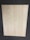 A large, rectangular piece of light wood with prominent grain patterns rests on a dark, textured floor. The wood surface appears smooth and flat with natural coloration and subtle variations in the wood grain.