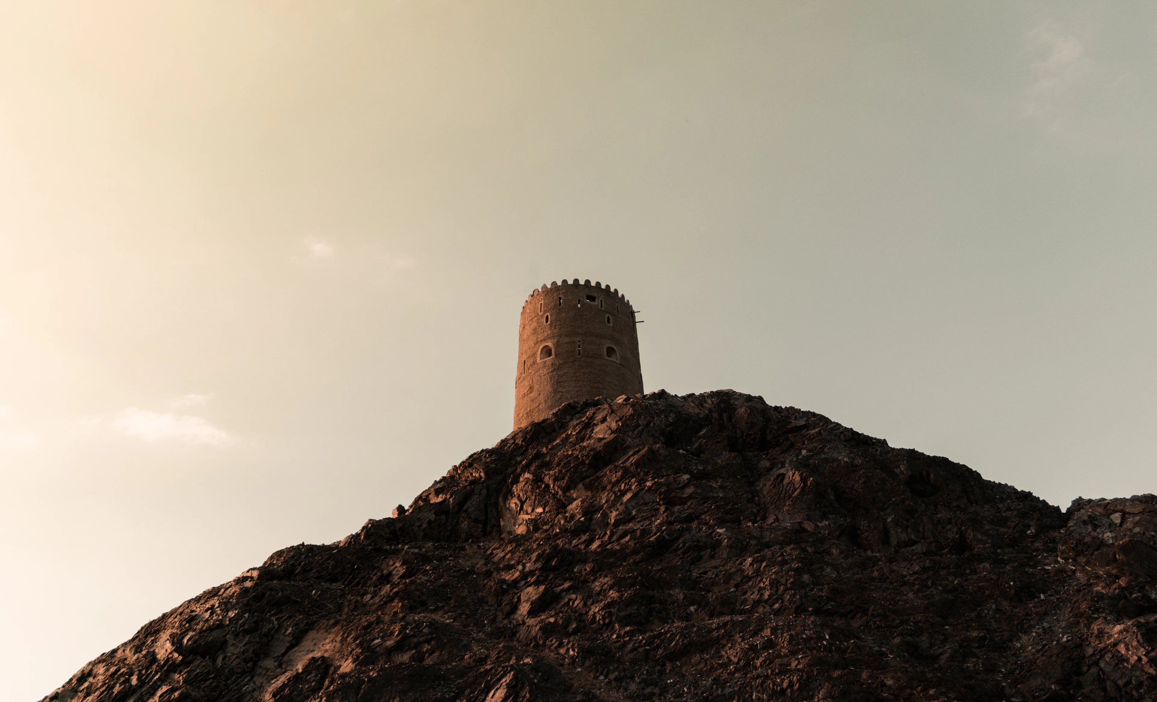A lone stone watchtower crowns a dark, rugged ridge under a warm golden sky.