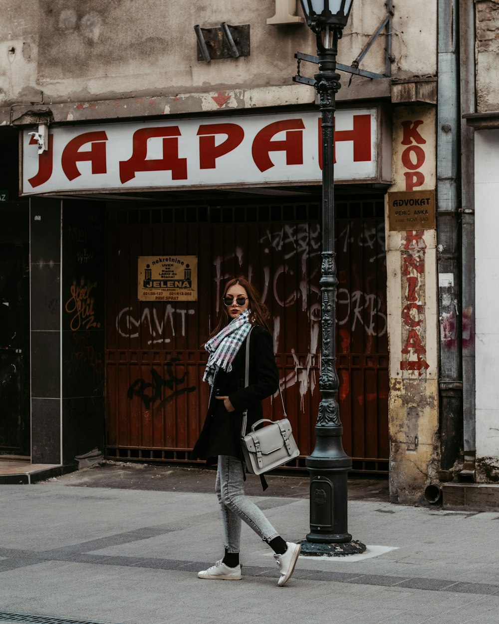 woman in black coat walking on street near post during daytime