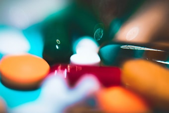 A colorful, abstract image featuring various pills and capsules in soft focus. The out-of-focus elements create a dreamy, almost surreal effect with light reflections and blurred shapes.