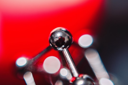 A close-up of a shiny, metallic structure that resembles a molecular model. The background features a vibrant red hue, with bokeh circles of light scattered across the image, creating an abstract, artistic feel.
