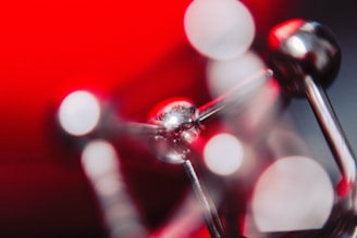 A close-up abstract image of a metallic molecular model with shiny spheres and rods set against a vibrant red background. The focus is soft, creating a dreamy and slightly blurred effect.