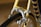 A close-up view of a bicycle brake system on a yellow frame, highlighting the metallic brake caliper and cable. The tire and part of the rim are visible, with spokes in the background. The frame features a decorative pattern of stripes in multiple colors.