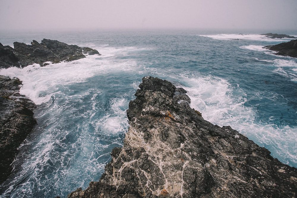 wave splashing on gray rocks during daytime