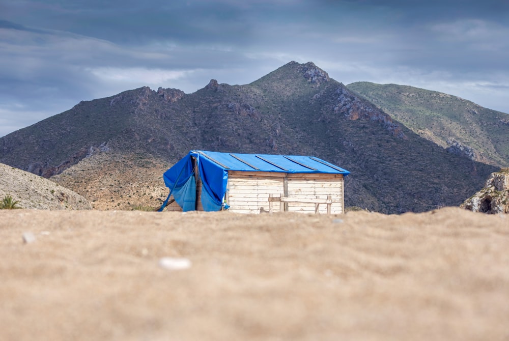 brown wooden shed with blue tarp roof beside mountain during daytime
