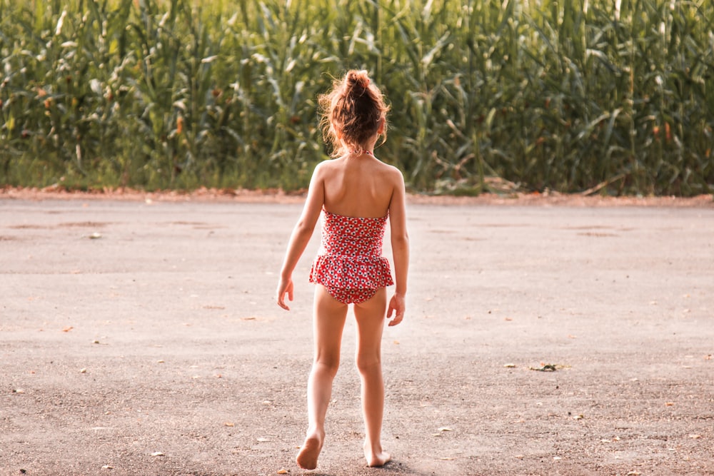 girl wearing onepiece standing beside corn plant during daytime