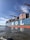 A large cargo ship is seen loaded with numerous shipping containers stacked neatly on its deck. The letters 'M O L' are prominently displayed on the side of the ship. Several cranes tower over the ship, indicating an active port environment. The water near the vessel is calm and a clear blue sky stretches overhead.