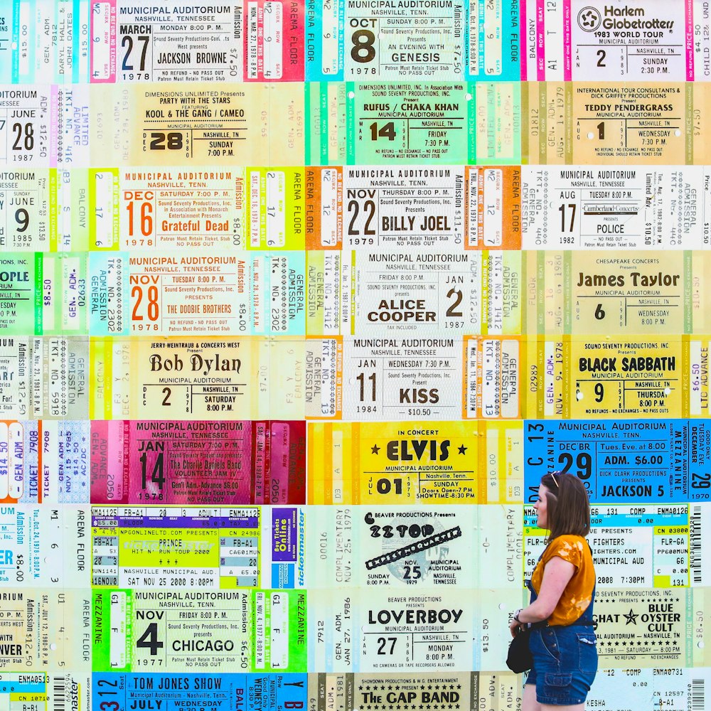 woman in blue jumpshorts beside assorted-ticket wall graffiti