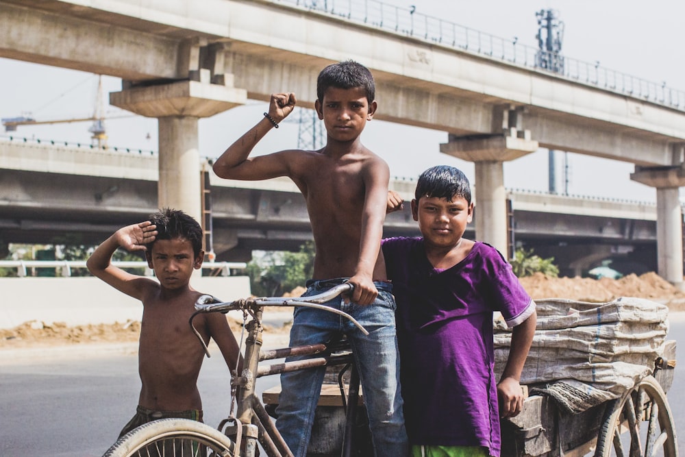 Tres niños levantando la mano derecha mientras montan en triciclo