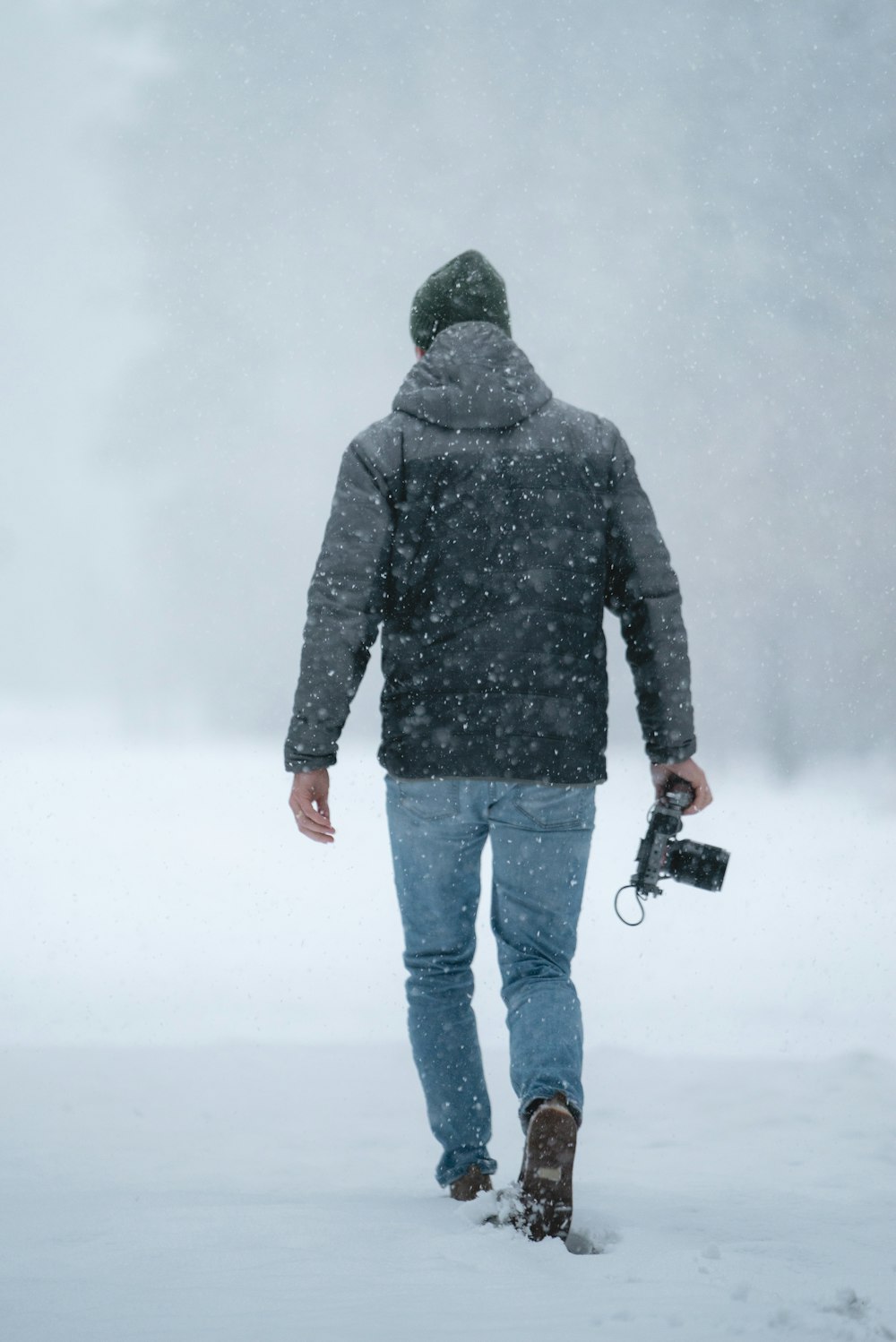 Mann in grauer Jacke hält Kamera beim Gehen auf Schnee