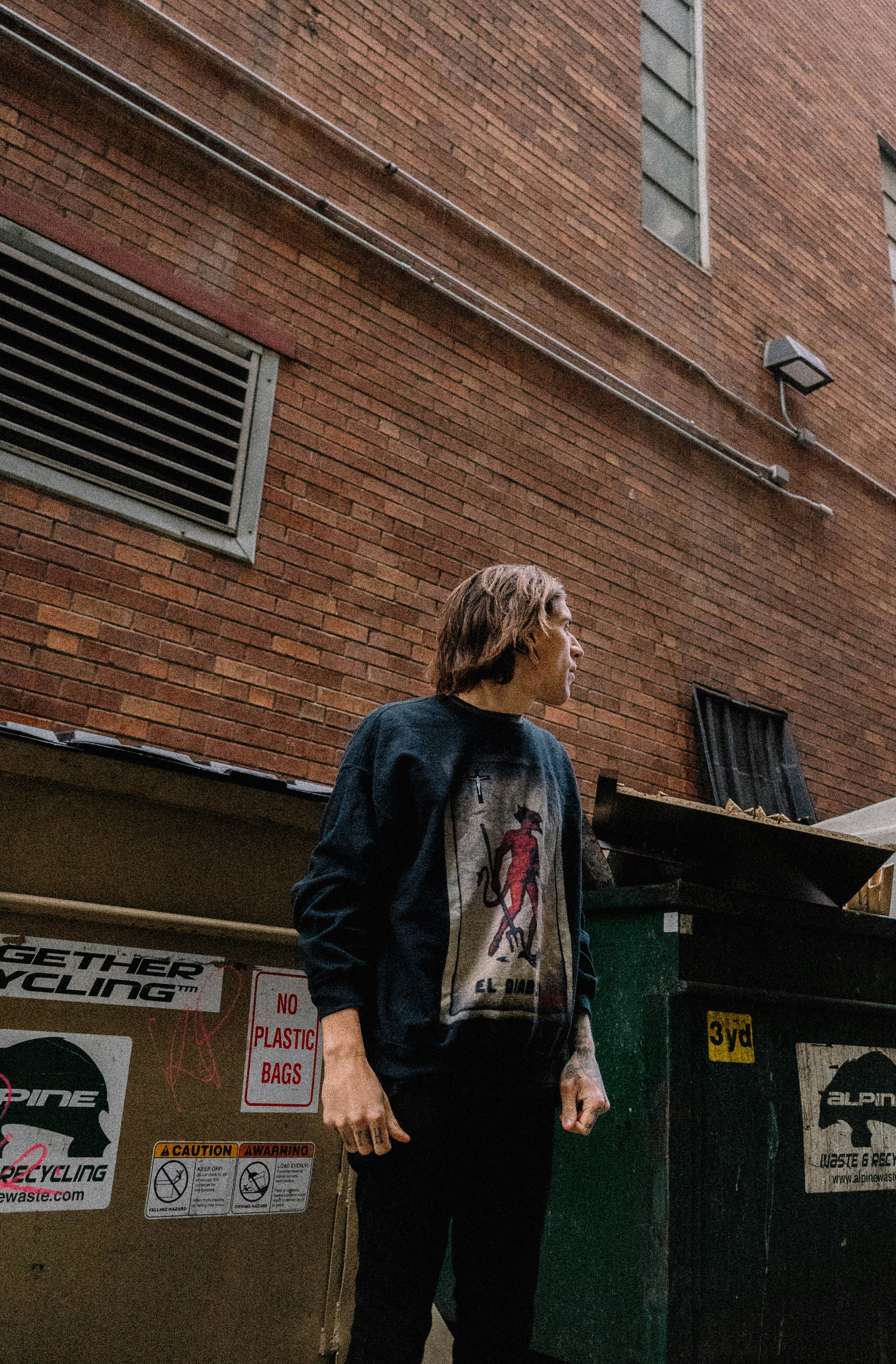 Man Standing Beside Building and Trash Bin