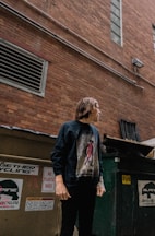 man standing beside building and trash bin