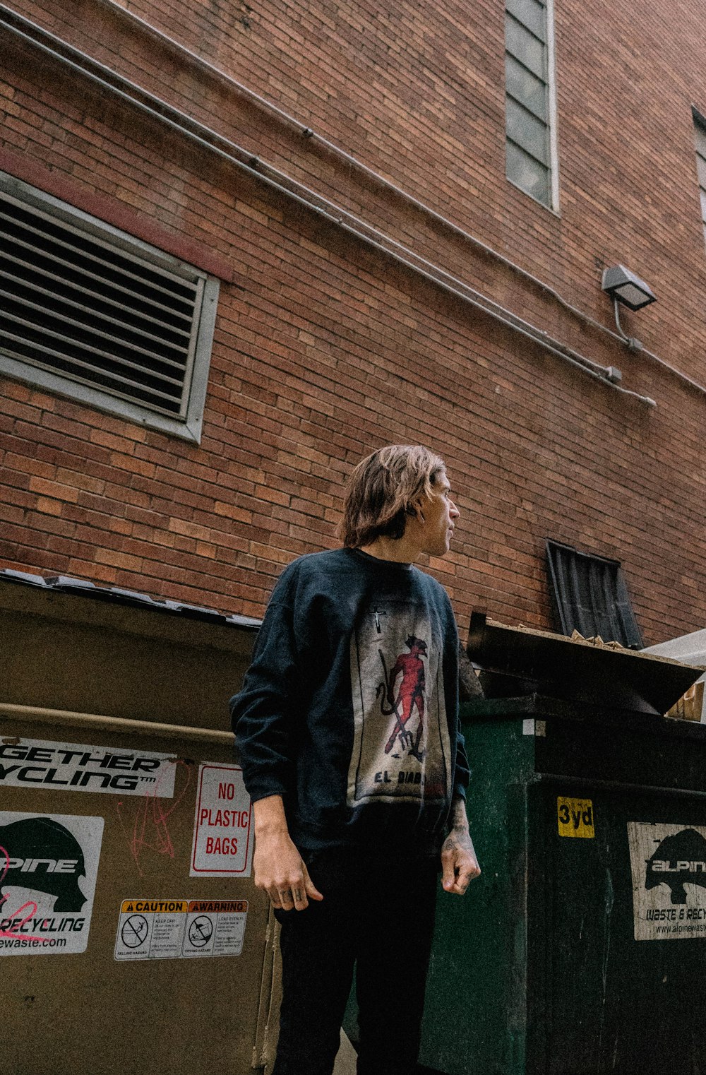 man standing beside building and trash bin