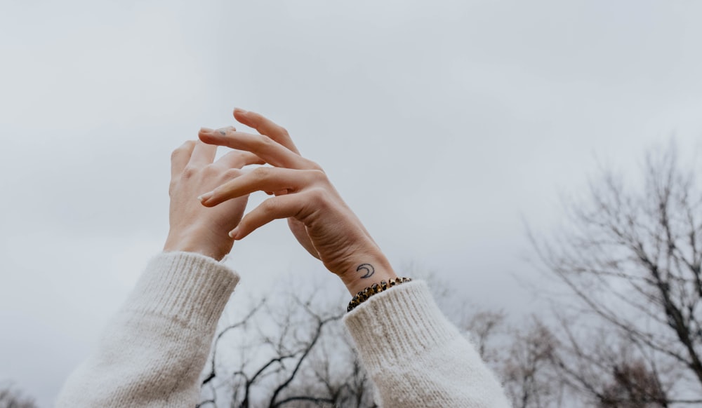 person wearing white sweater raising hands under white sky