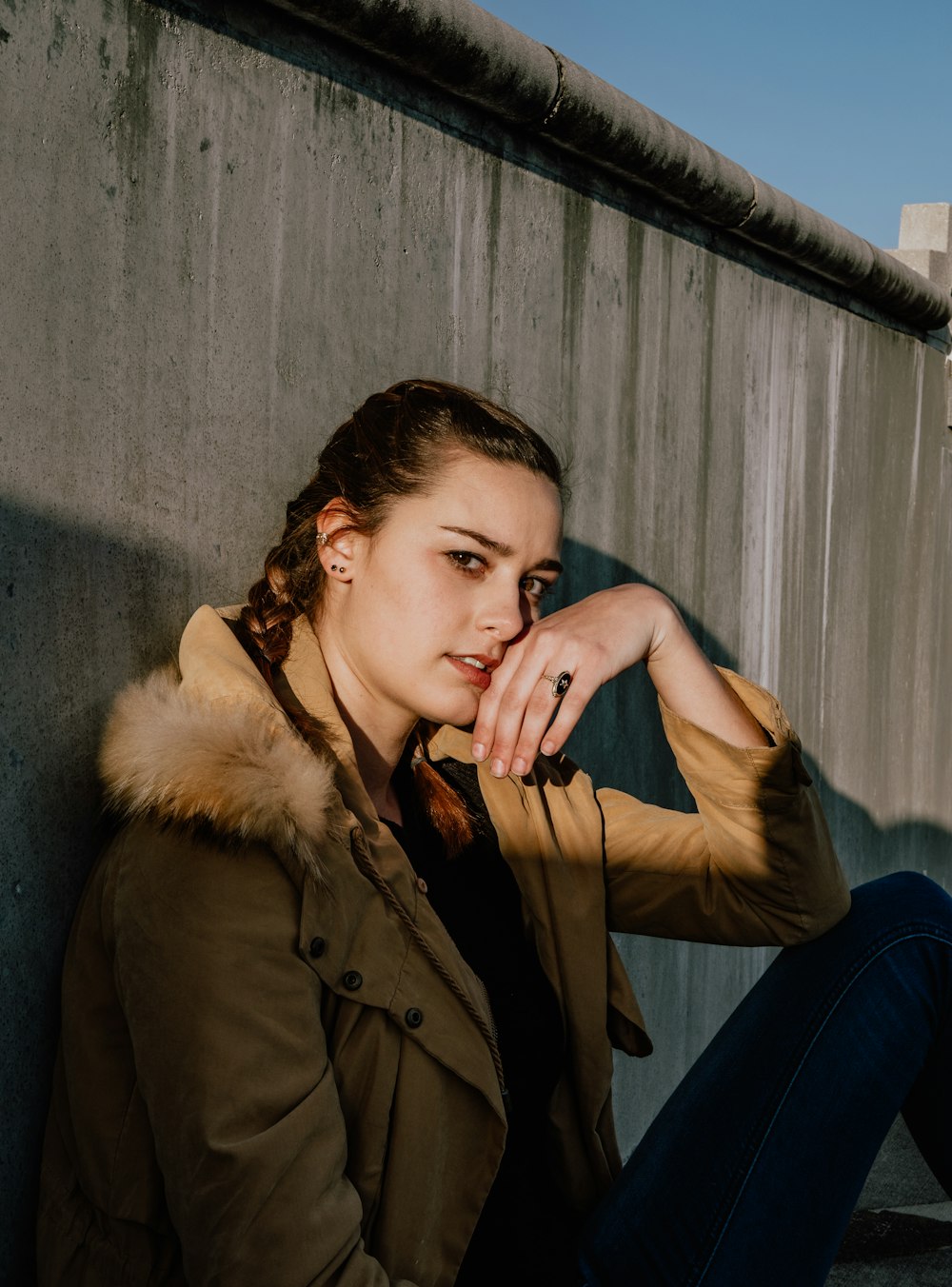 mulher na jaqueta marrom do decote da pele sentada na frente da parede de concreto