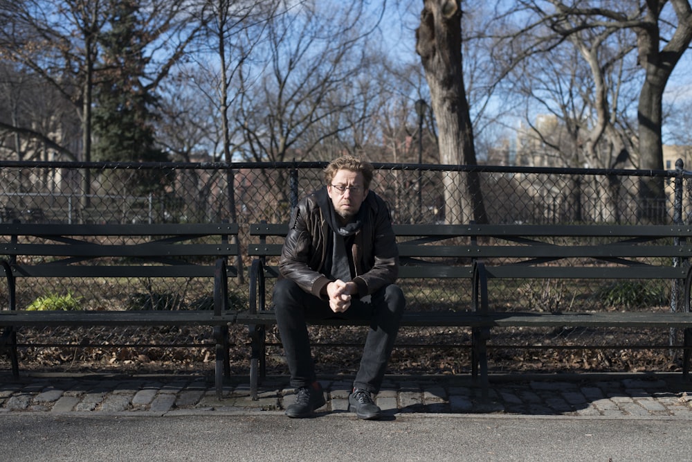 man sitting on park bench under leafless tree