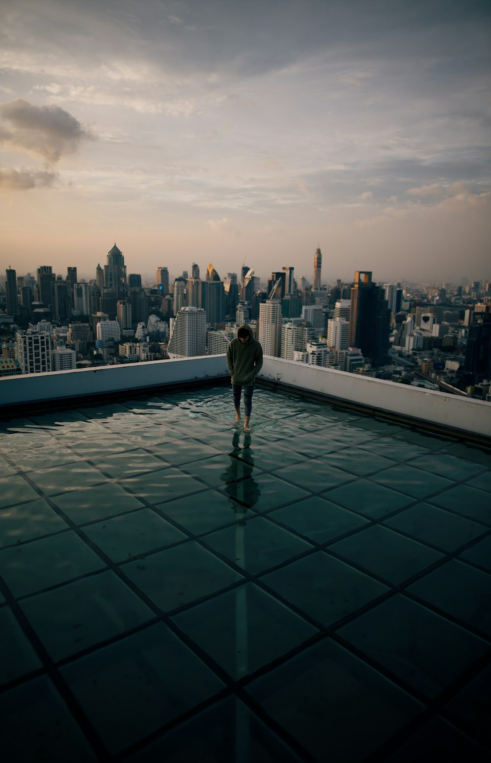 회색 하늘 아래 고층 건물을 마주보고 있는 건물 꼭대기에 서 있는 남자