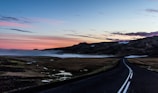 View of freshly paved, smooth asphalt road extending through rolling hills at sunrise.