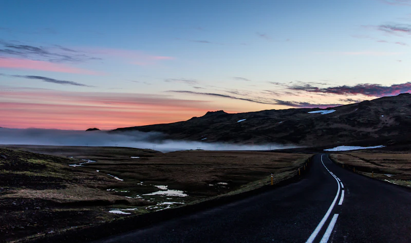 Iceland's Ring Road curving through a lava field at sunset with low fog and a pink and orange sky