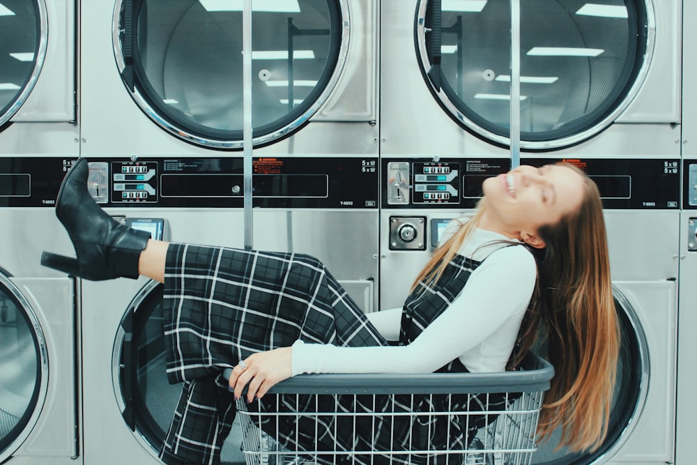 smiling woman in black dress sitting in basket near front-load washers