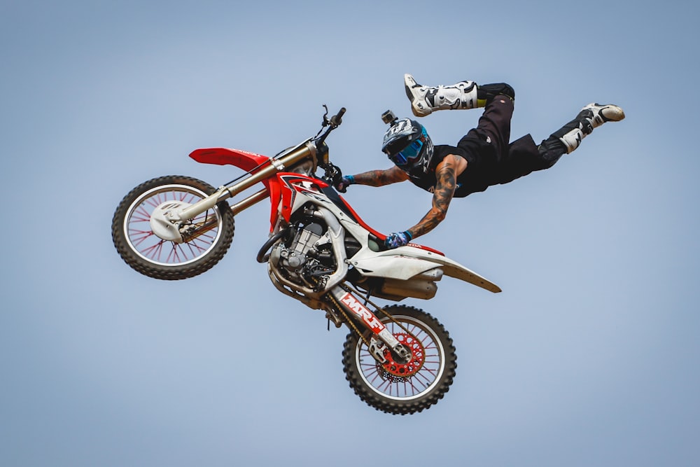 Jinete masculino con tatuajes en el brazo montando moto de cross haciendo truco en el aire durante el día