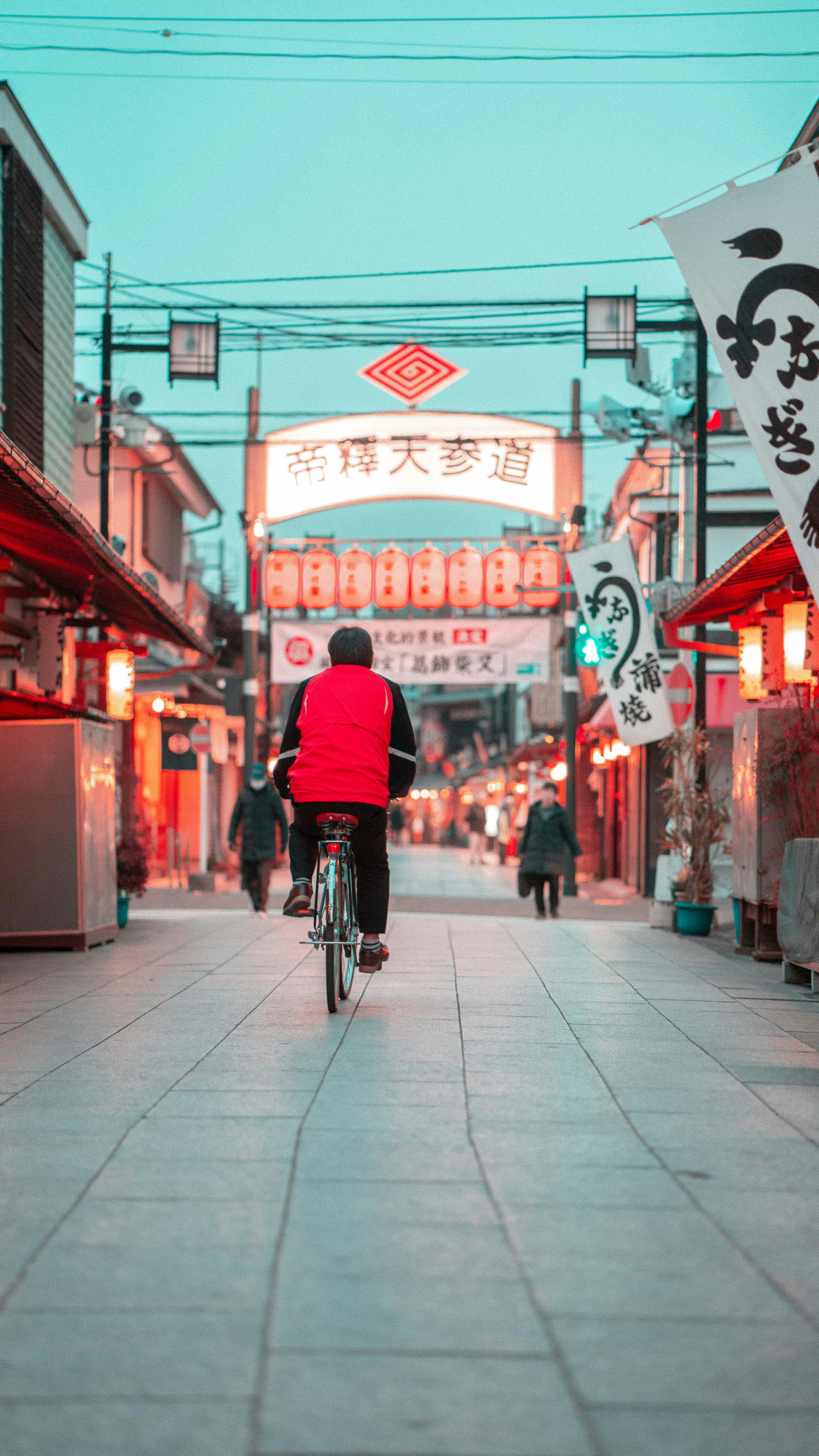 person cycling on streets with Kanji signs during daytime