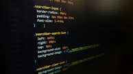 A screenshot of CSS code on a dark background, featuring styling rules for search bar elements such as border-radius, padding, and font size. Colored highlights emphasize syntax, with properties and values outlined in purple, orange, and green.