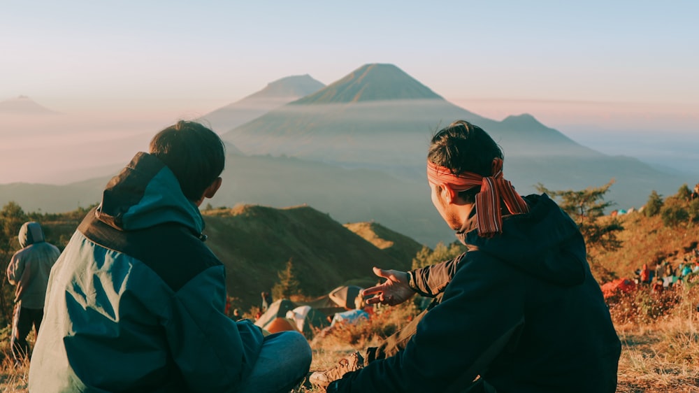 two men sitting and facing green mountain