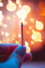 A glowing matchstick with tiny heart sparks above a small matchbox featuring a pizza slice logo, set against a soft peach and white Amalfi Coast-inspired background.