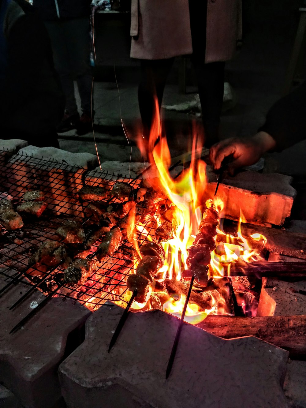 person grilling on bonfire surrounded by people