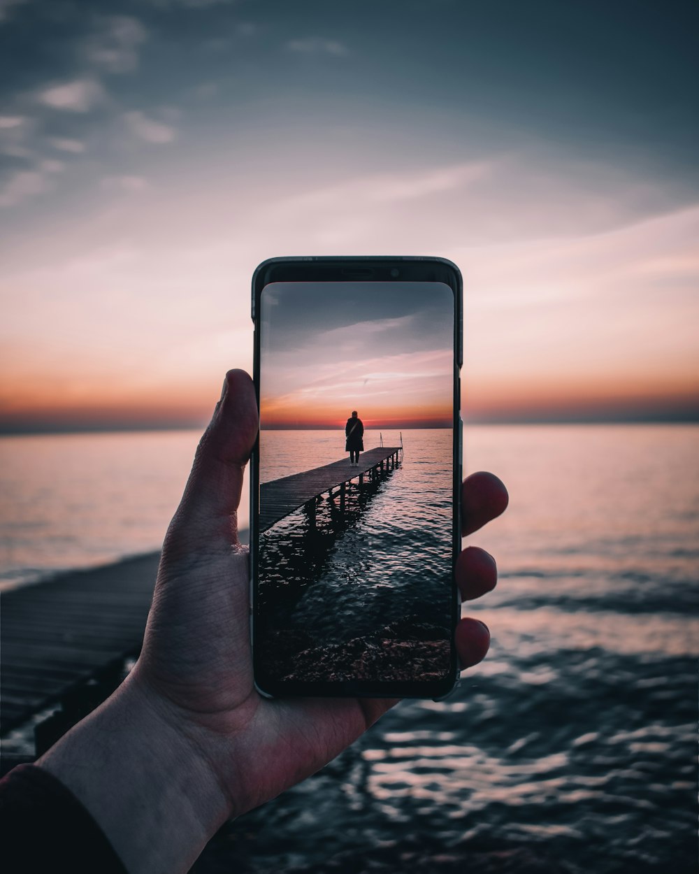 smartphone displaying person standing on dock during golden hour