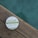 A round container of hemp whipped body butter is placed on a wooden surface. The label highlights that it contains organic certified ingredients and promotes its properties such as being an antioxidant and skin conditioner. The background features a calming, blurred teal color.