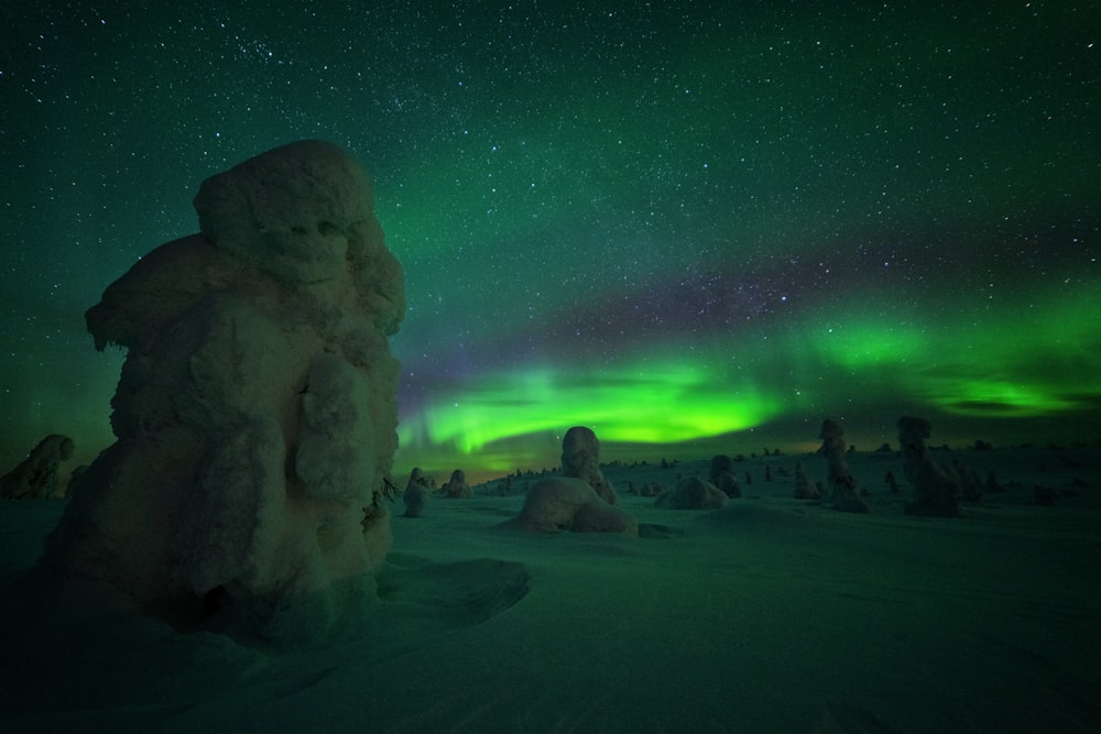 formações rochosas cobertas de neve à noite durante a aurora boreal