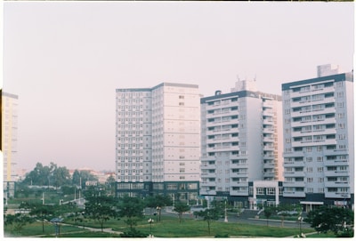 Several mid-rise apartment buildings with a uniform architectural style, featuring numerous windows and balconies, are lined up next to each other. The buildings are surrounded by small park areas with green lawns and scattered trees. The sky is overcast with a soft light, contributing to a calm atmosphere.