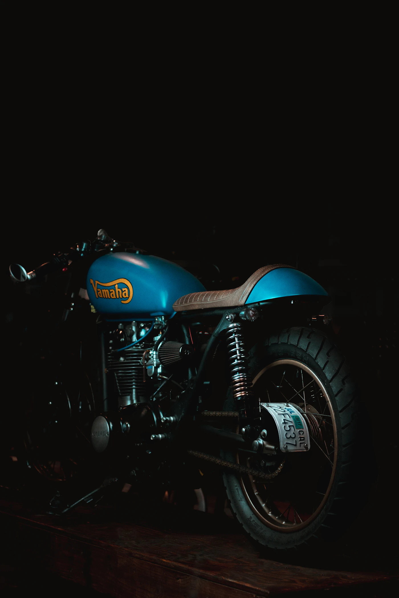 Teal and cream cafe racer parked against a raw concrete wall