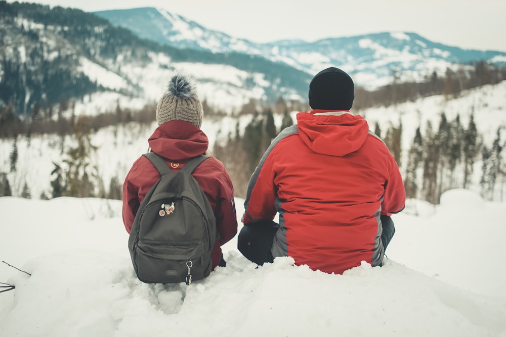 man and woman sitting on snowfield