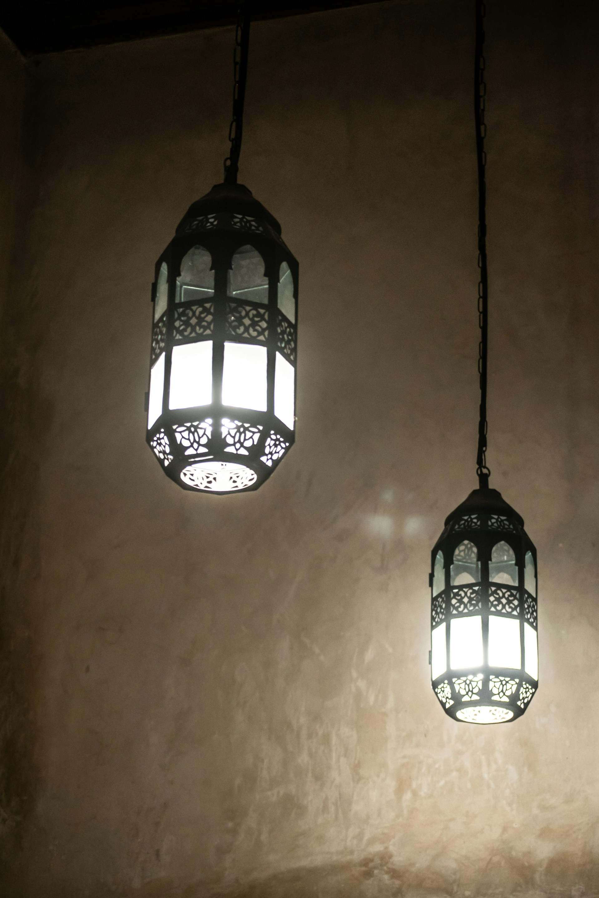 Elegant Moroccan lanterns with detailed metalwork casting delicate shadows in a minimalist modern interior with black and gold accents.