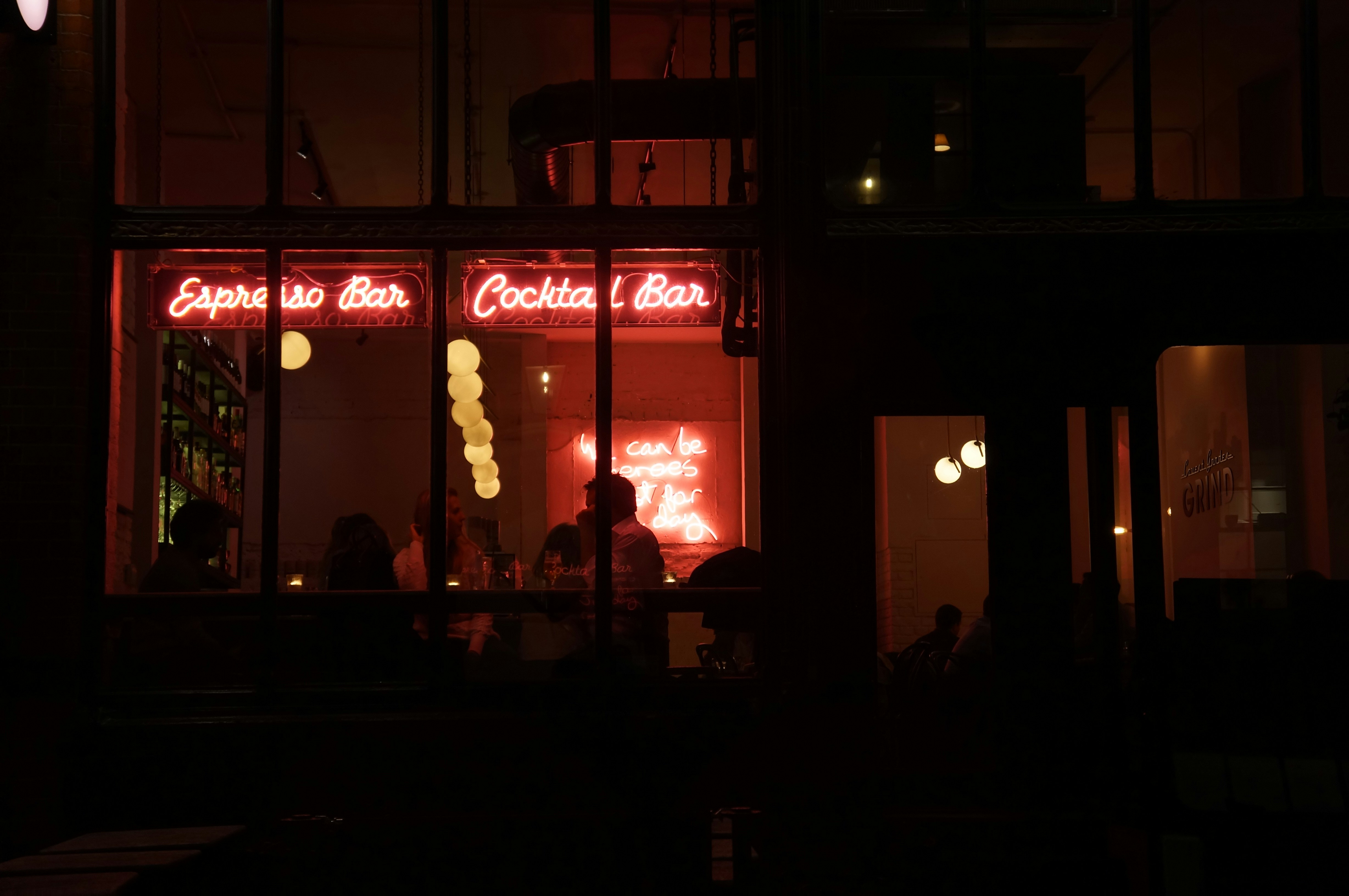 people sitting inside building with red neon signage, 