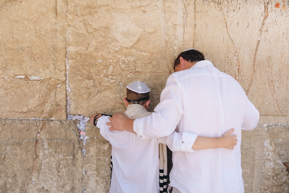 two men in white top standing beside wall