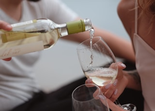 person pouring liquor from clear glass bottle into wine glass