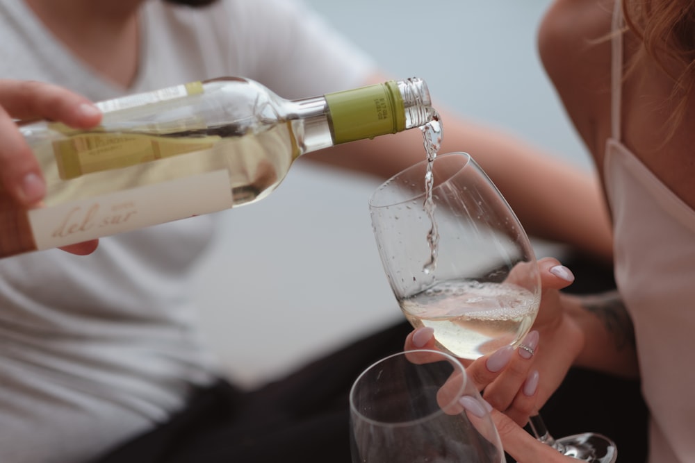 person pouring liquor from clear glass bottle into wine glass