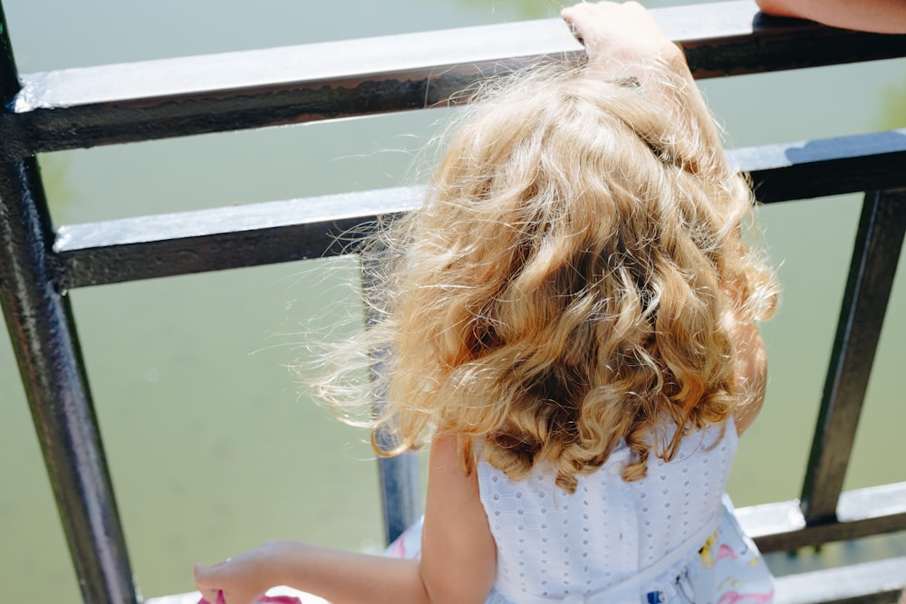 girl wearing white dress holding on to black fence